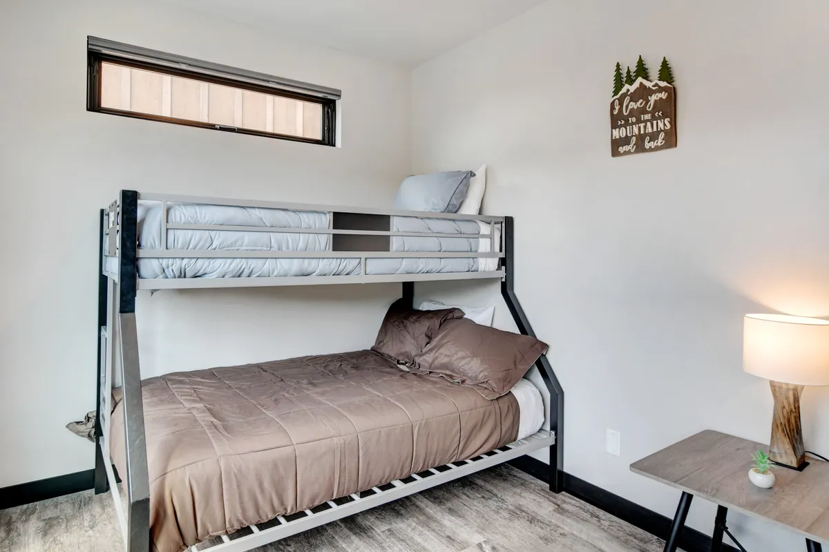 A cozy bunkroom with twin-over-full bunk beds, a nightstand, a lamp, and playful decorative touches. The space is inviting and designed for families or young guests to enjoy restful sleep or relaxed moments.