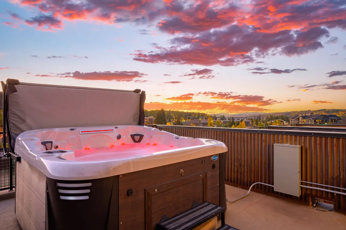 A tranquil rooftop hot tub scene at sunset, overlooking the cityscape and surrounding mountains. The warm glow of dusk enhances the inviting atmosphere, suggesting relaxation after an action-filled day.