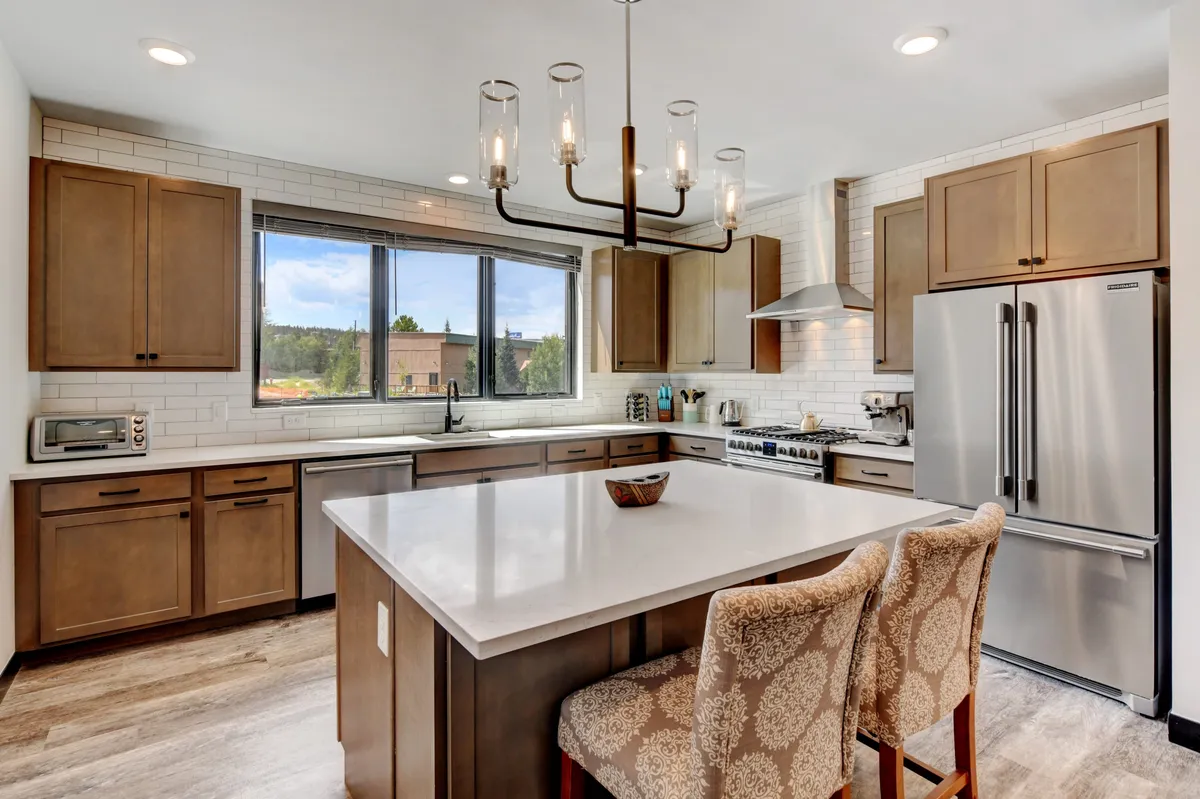 A welcoming kitchen scene with a central granite island featuring ample seating, large windows admitting abundant natural light, and sleek modern appliances. The spacious layout is ideal for both cooking and socializing, with enough room for guests to gather around the island.