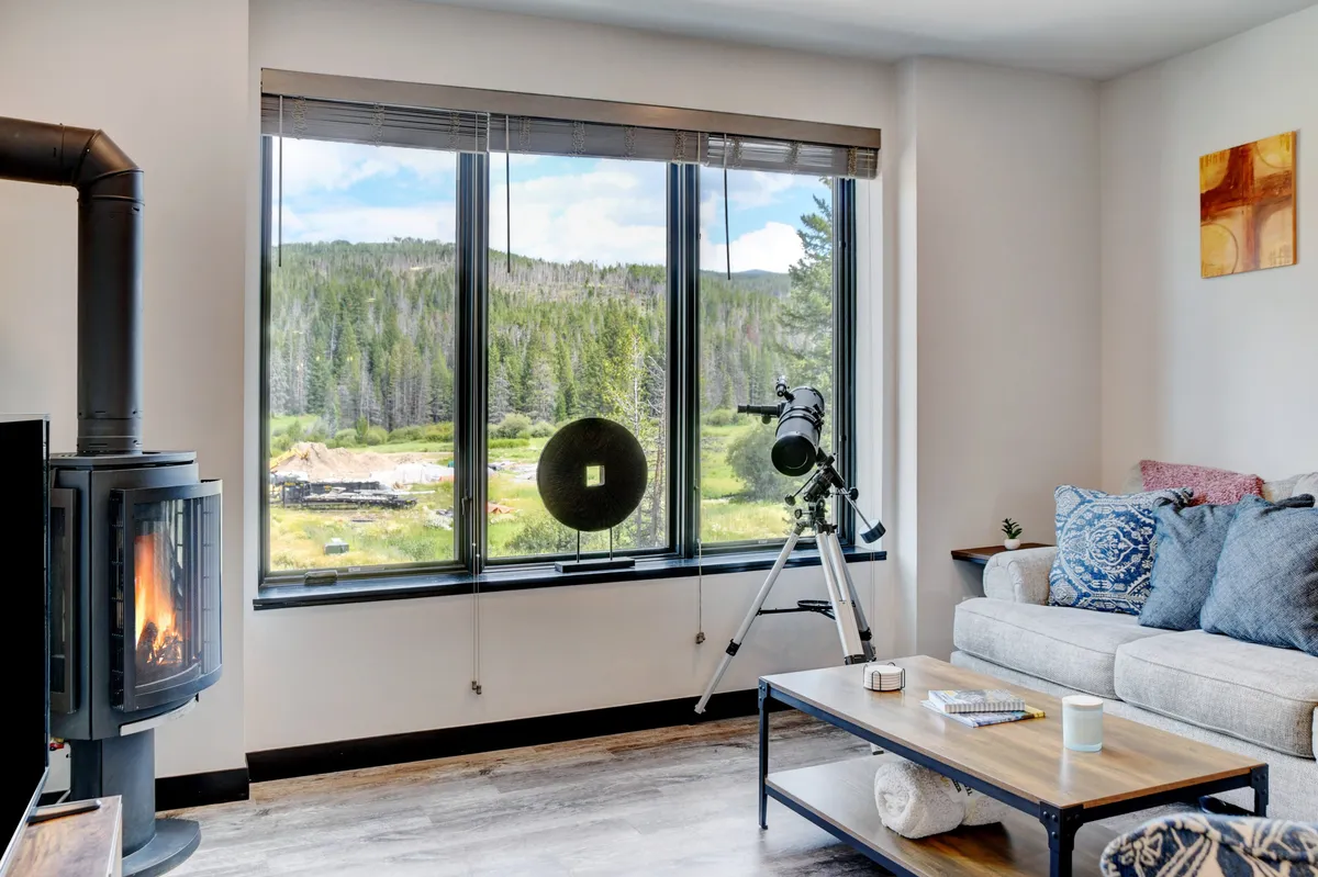 A serene living room with large windows overlooking the landscape, a telescope positioned by the window, a cozy sofa, and a fireplace. The space exudes comfort and inspires relaxation or focused work.