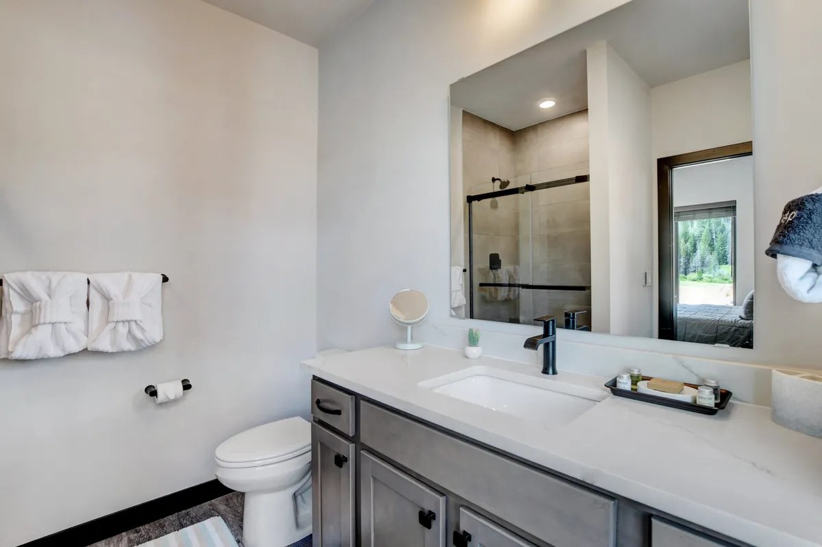 A bright bathroom with a modern vanity, large mirror, and glass shower enclosure. The layout is clean, organized, and inviting, echoing the convenience of a full bathroom for each bedroom.